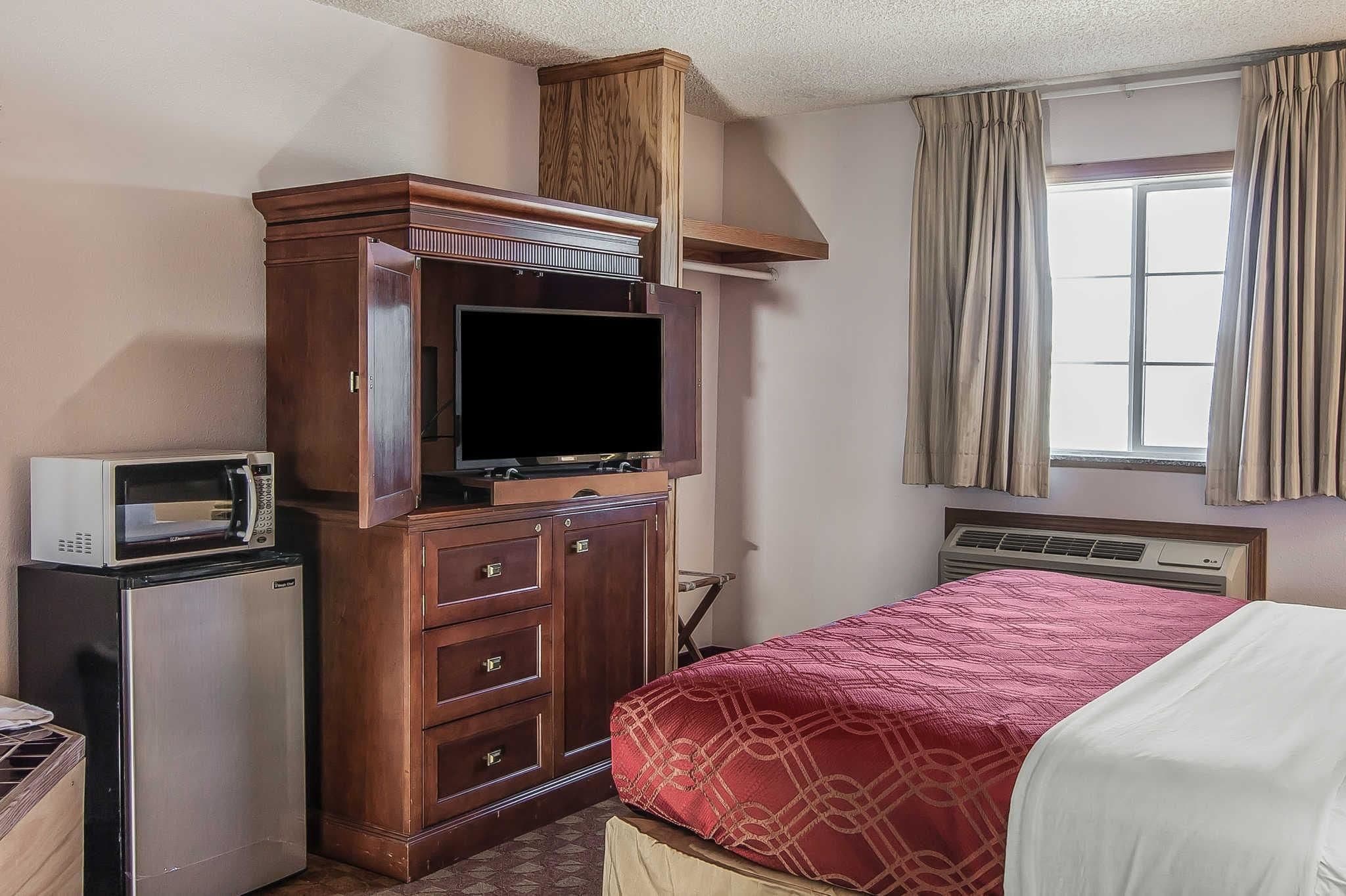 A hotel room with a bed, a wooden cabinet with a television, a microwave, and a small refrigerator.