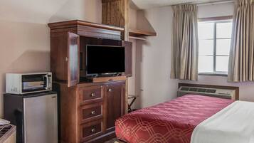 A hotel room with a bed, a wooden cabinet with a television, a microwave, and a small refrigerator.