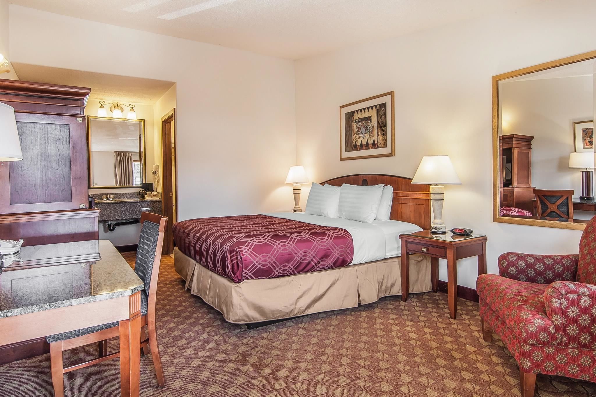 A hotel room with a bed, a desk, a chair, a dresser, and a mirror.