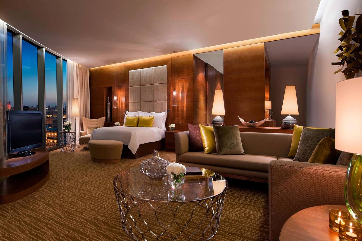 A modern hotel room with a large bed, a sofa, a TV, and a glass coffee table.