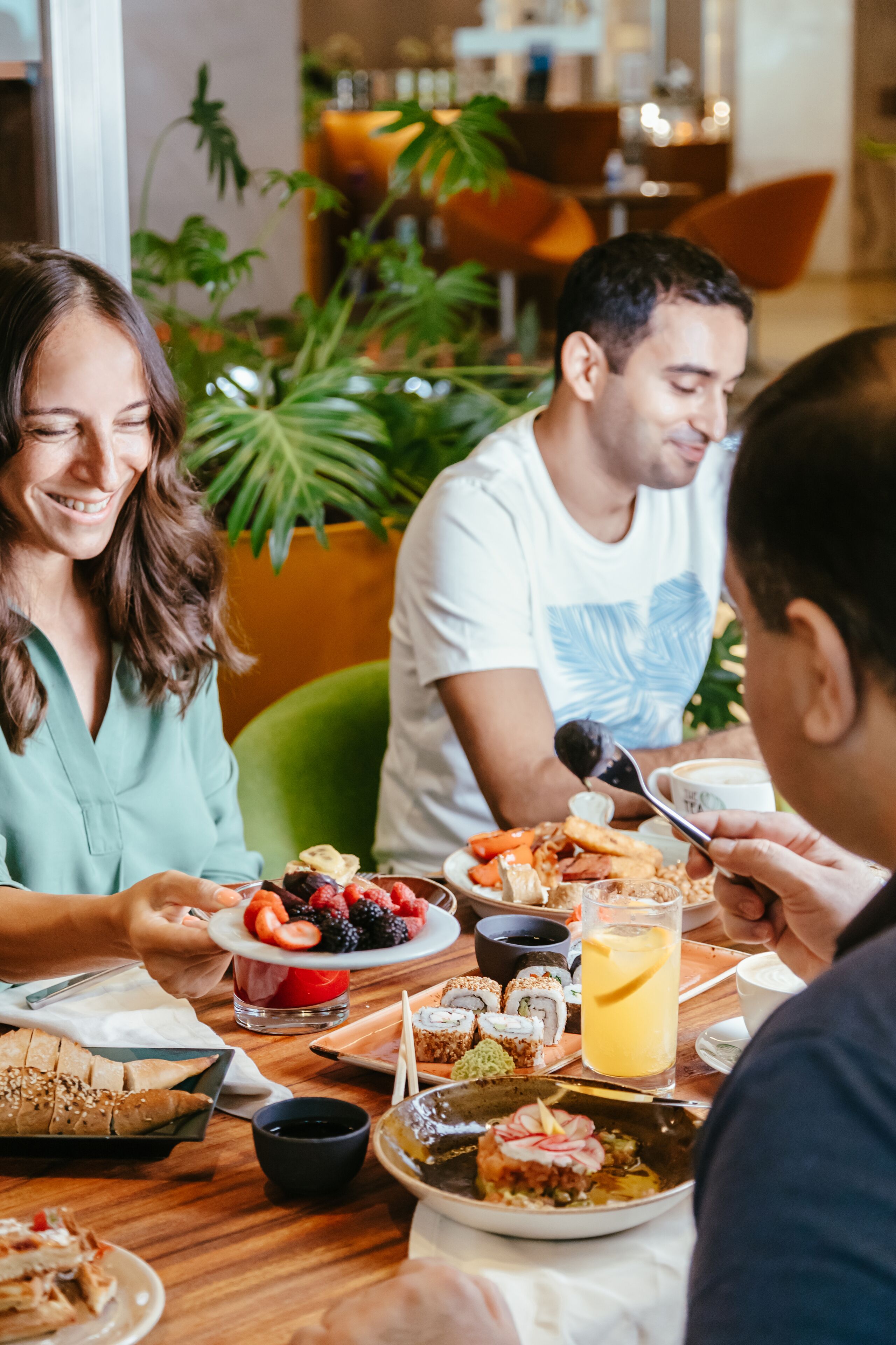 Una mesa de comedor con varios platos, entre ellos sushi, fruta y un vaso de zumo de naranja.