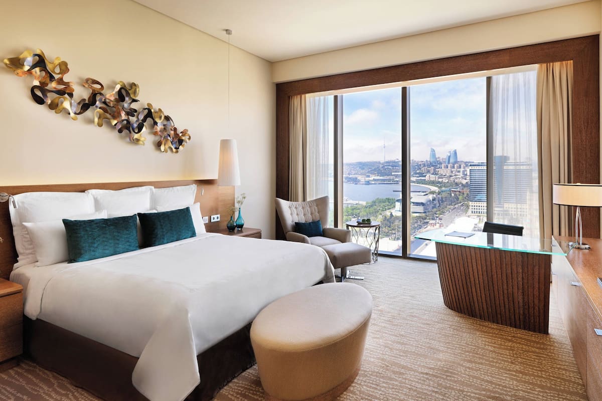 A hotel room with a large bed, a desk, and a view of a cityscape.