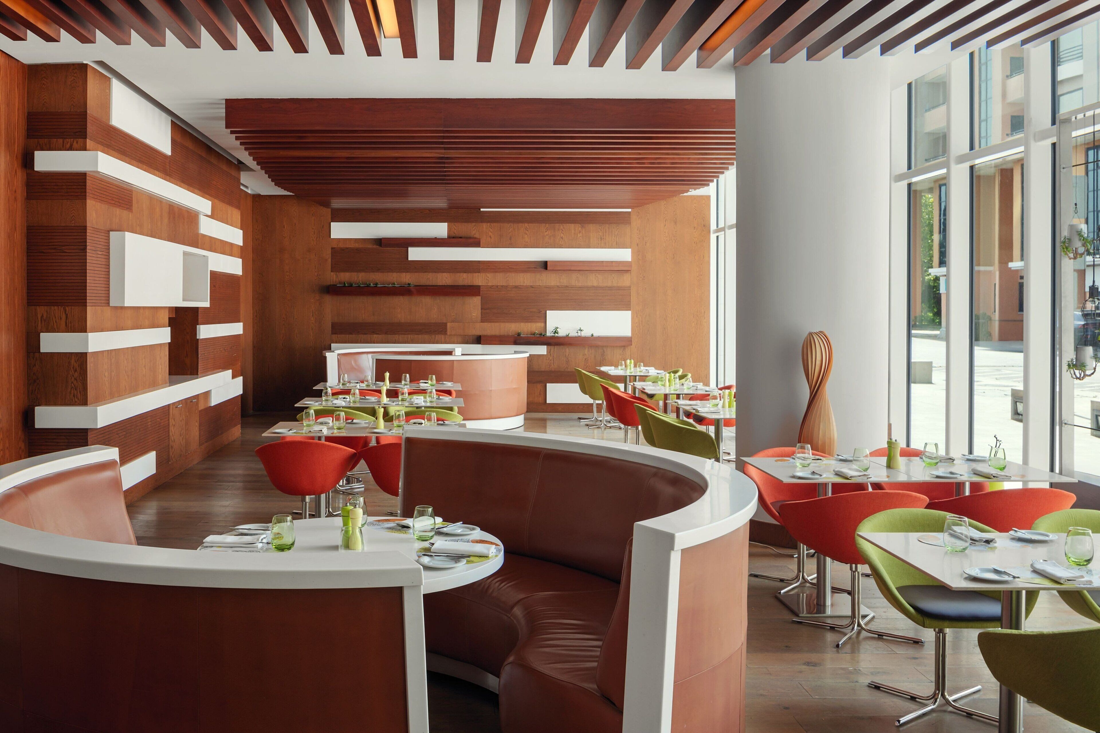 A modern restaurant interior with curved seating, wooden panel walls, and large windows.