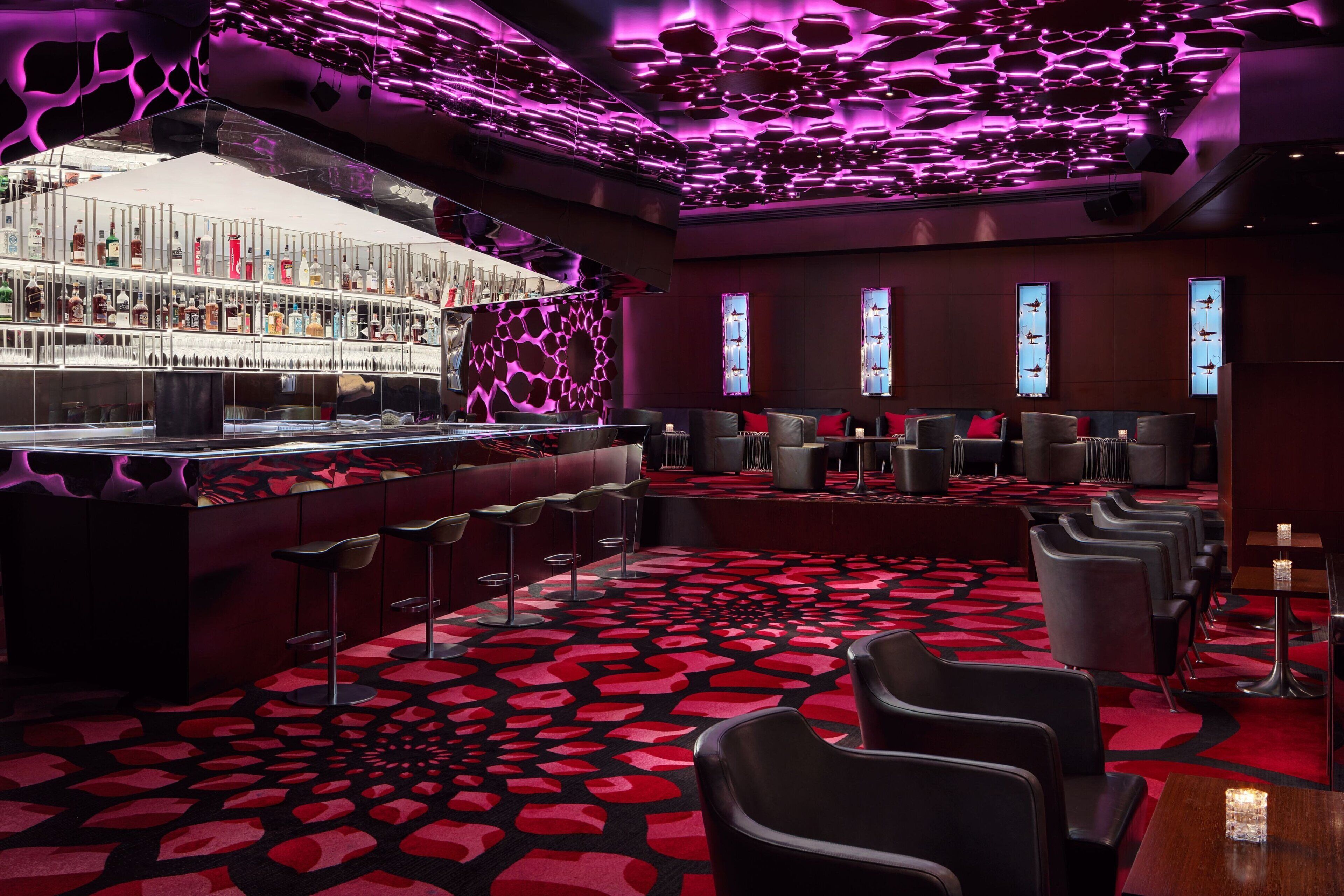 A bar area with a red patterned carpet, bar stools, and a well-lit bar counter.