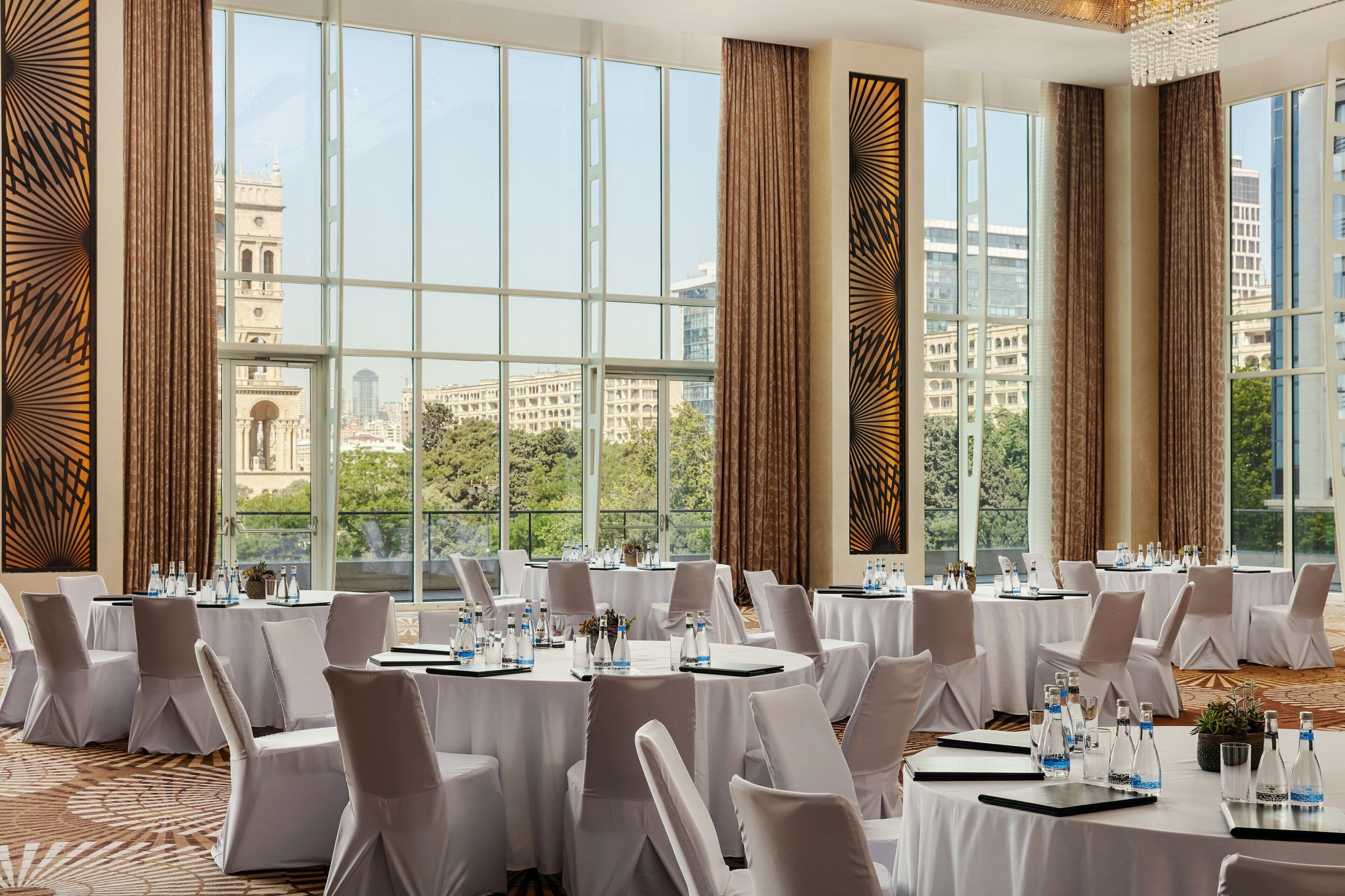 A conference room with round tables, white chairs, and a city view through large windows.