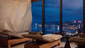A spa room with two massage tables, a large window offering a city view, and a small table with a plant. - JW Marriott Absheron Baku (Baku)