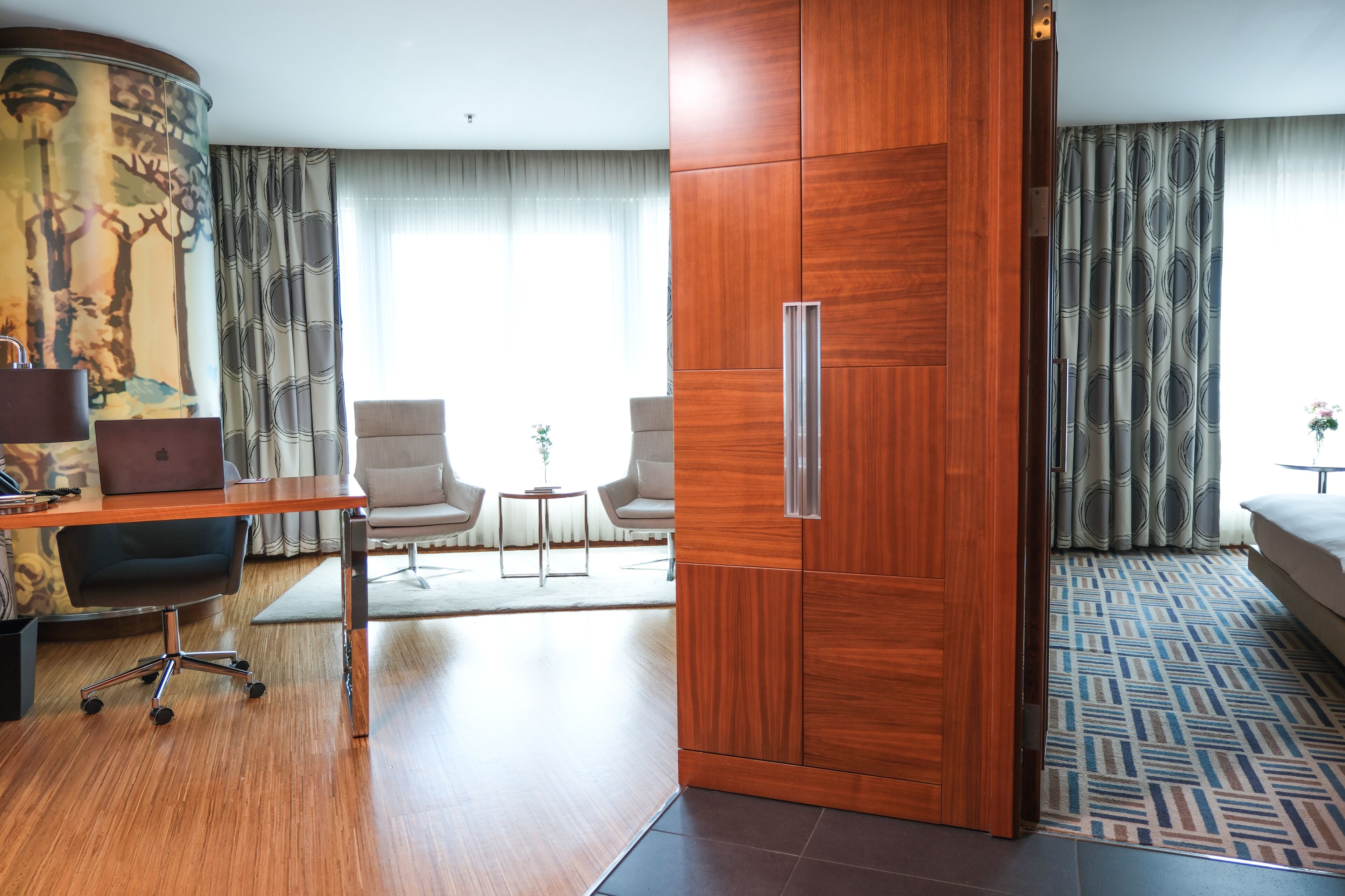 Een hotelkamer met een houten bureau, twee stoelen, een bed, een kledingkast en een kamerbreed tapijt met dessin.