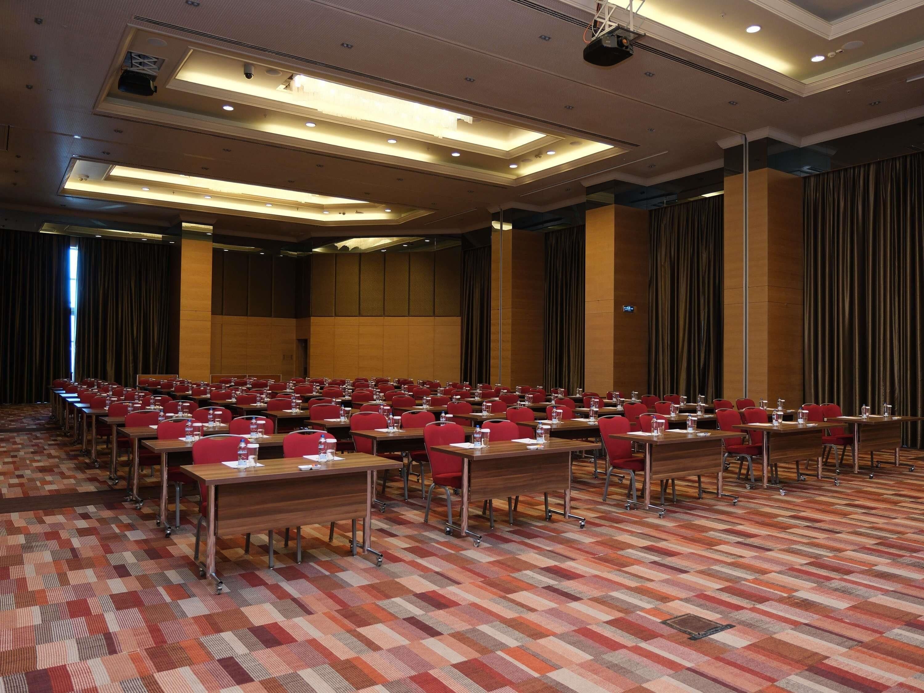 A conference room with rows of tables and chairs, equipped with microphones and water bottles.
