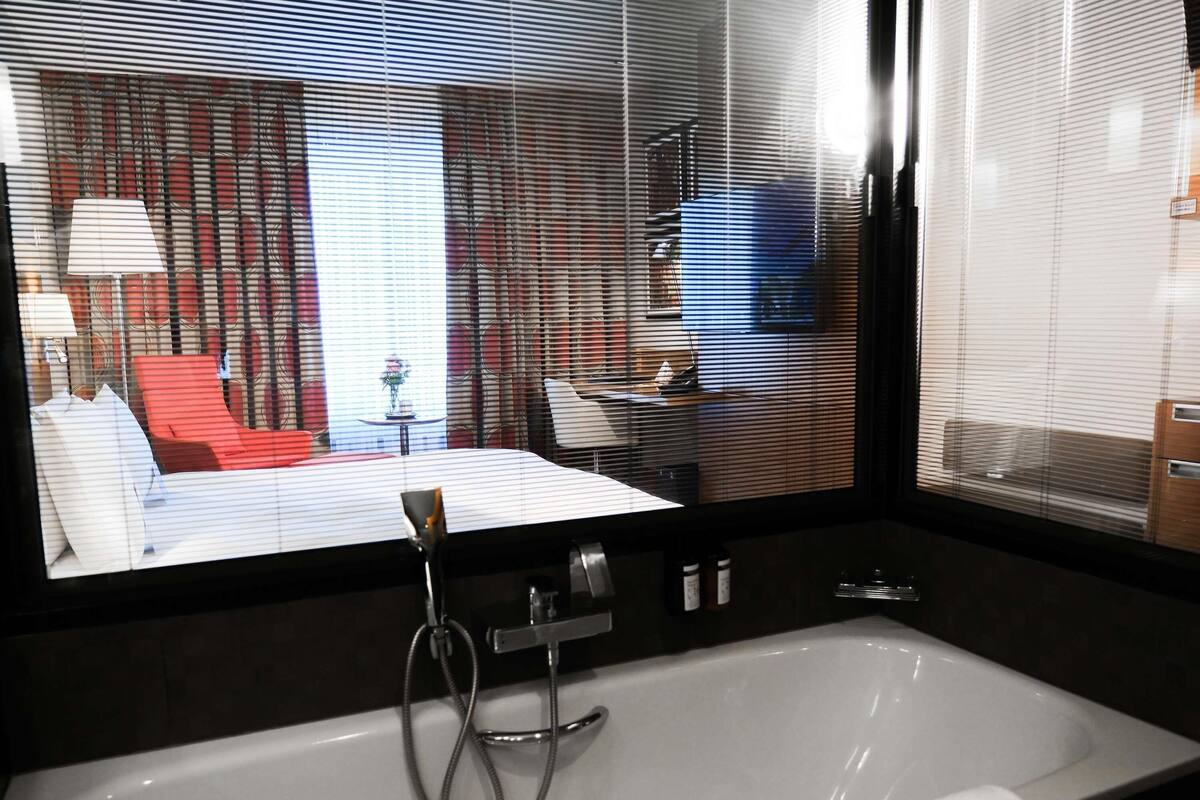 A modern bathroom with a bathtub, a shower, and a window with blinds.