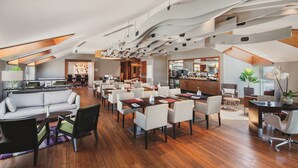 Un amplio salón con diseño moderno, que ofrece una variedad de opciones de asiento, incluyendo sofás y mesas, y una cocina al fondo.