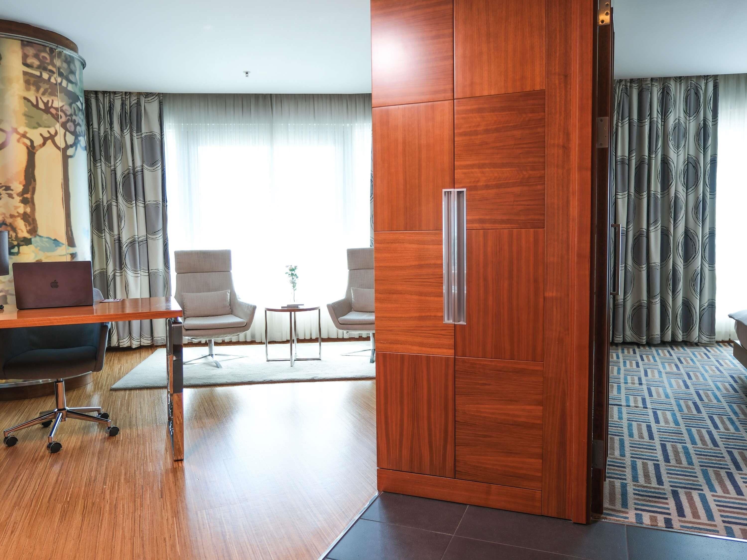Ein Hotelzimmer mit Schreibtisch aus Holz, zwei Stühlen, einem Laptop, einem kleinen Tisch mit einer Vase und einem großen Kleiderschrank.