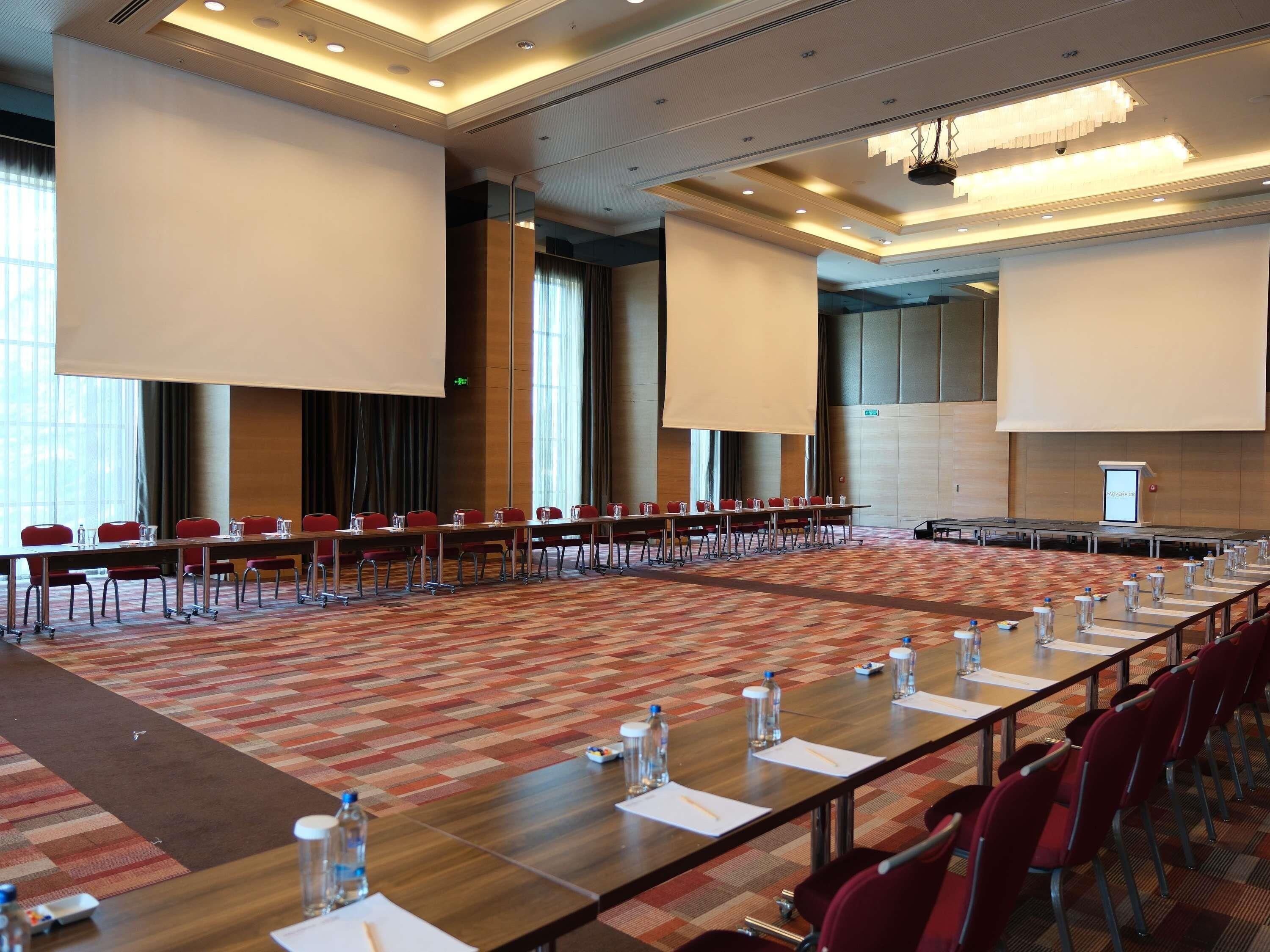 Une salle de conférence avec de longues tables, des chaises rouges et un sol recouvert de moquette.