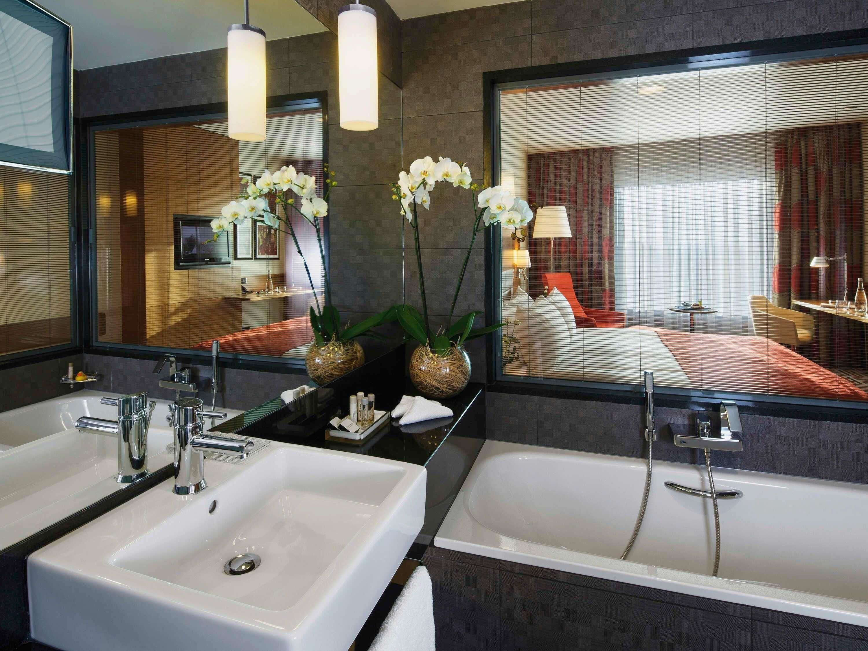 Un baño moderno con dos lavamanos, una bañera y un espejo grande que refleja un dormitorio.