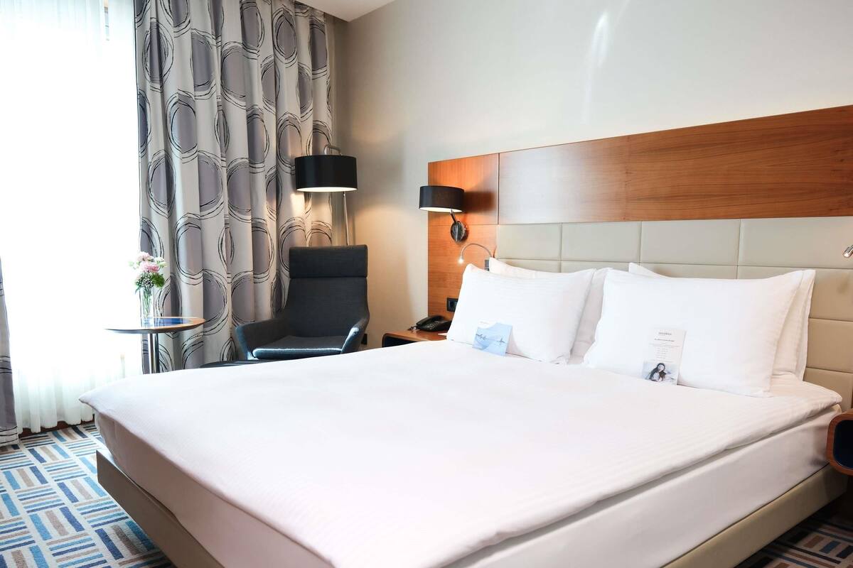 A hotel room with a large bed, a chair, a nightstand, and a lamp.
