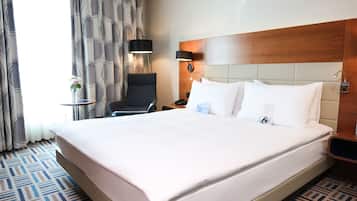 A hotel room with a large bed, a chair, a small table, and a lamp.