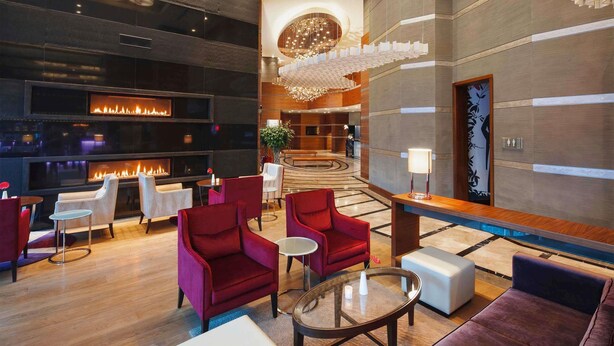 Un vestíbulo moderno con chimenea, asientos de color rojo y blanco, una araña y una mesa de recepción.