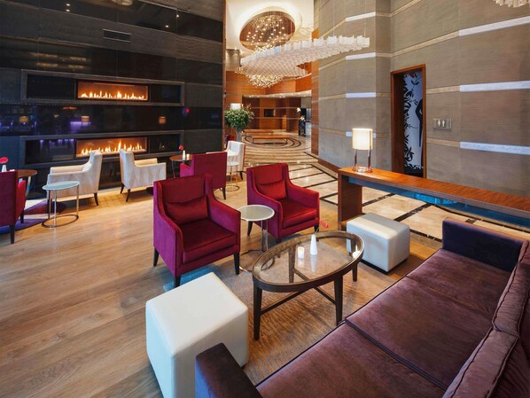A modern lobby with a fireplace, red and white seating, a chandelier, and a reception desk.