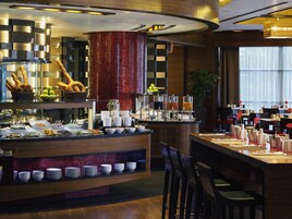 Um lobby de hotel moderno com área de bar central, espaços para sentar e uma coluna decorativa vermelha.