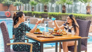 Dos personas cenando en una mesa junto a una piscina, con varios platos y bebidas.