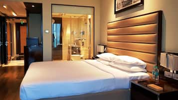A hotel room with a large bed, bedside table, and a bathroom visible through a glass partition.