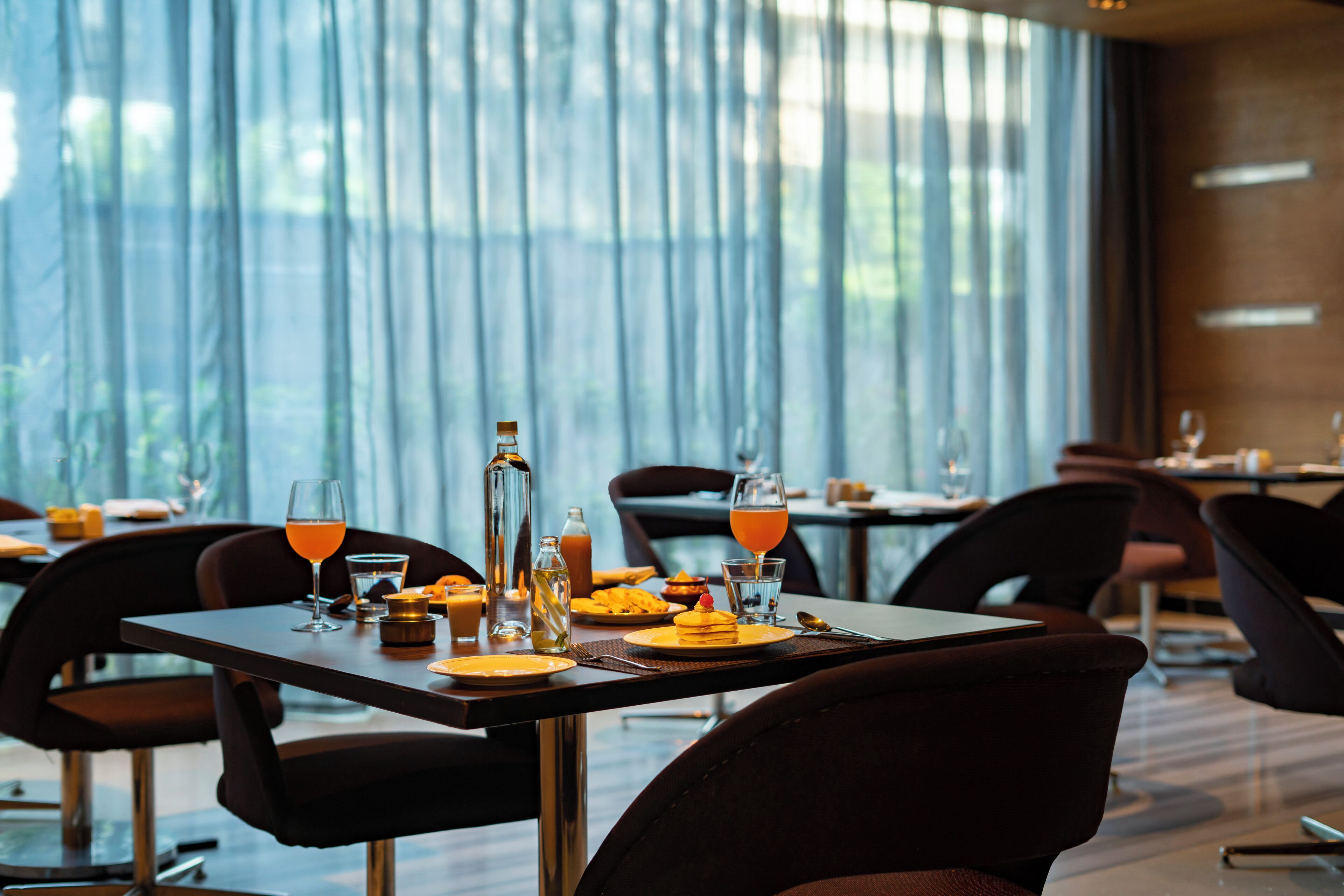 A restaurant with tables set for dining, featuring a view through large windows.