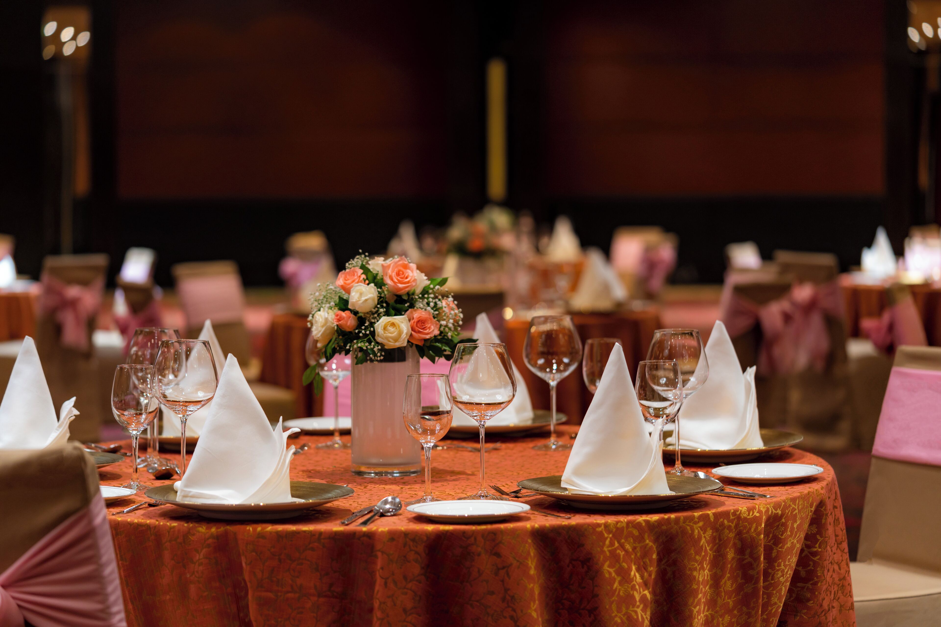 A banquet table set with white napkins, wine glasses, and a vase of flowers.