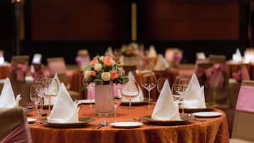 A banquet table set with white napkins, wine glasses, and a vase of flowers.