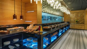 Un área de bufé con diversas opciones de comida, una barra con salpicadero de azulejos y lámparas colgantes.