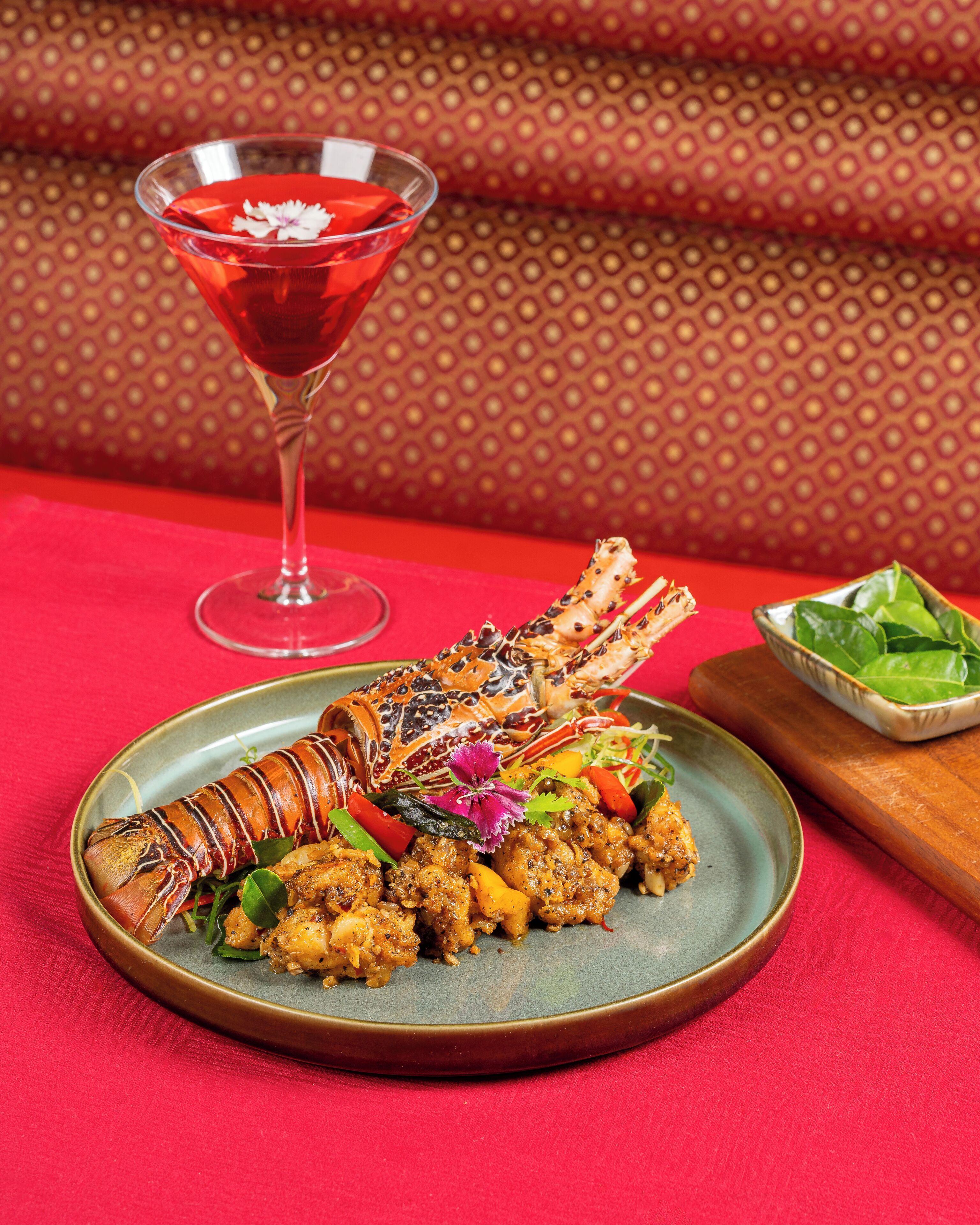 A plate of cooked lobster with vegetables and a martini glass in the background.