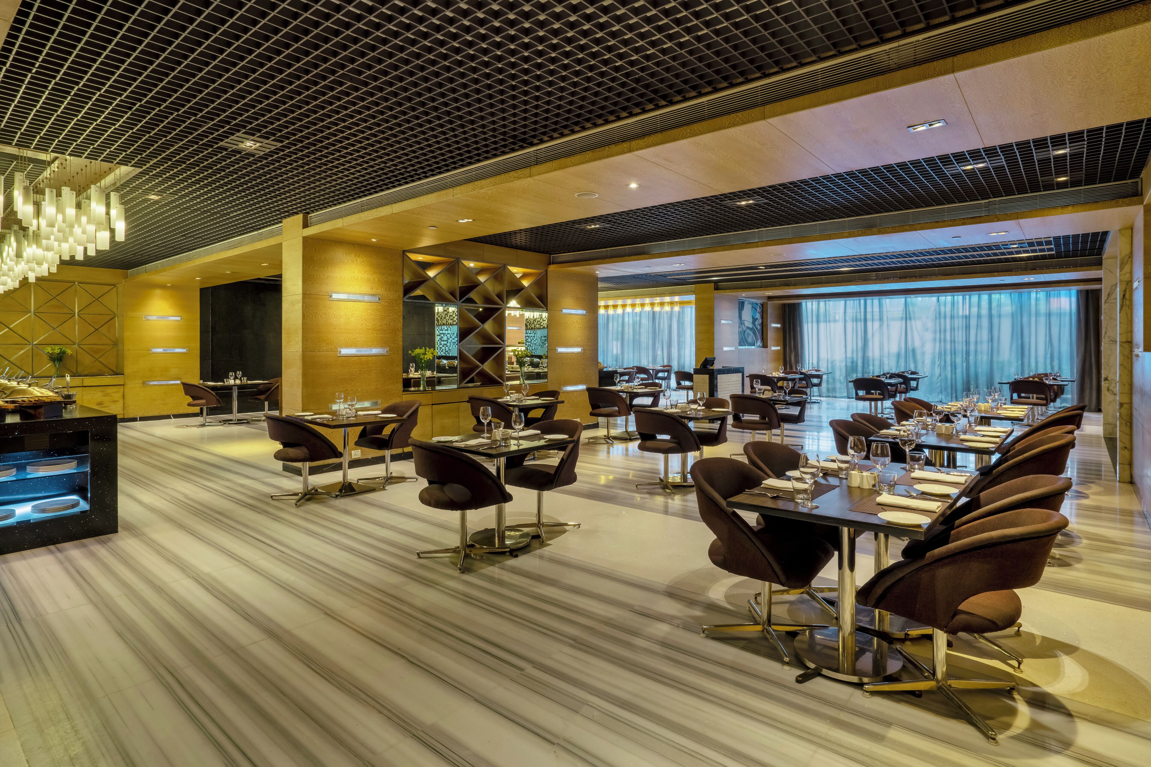 A modern hotel dining area with marble flooring, contemporary furniture, and a central bar area.