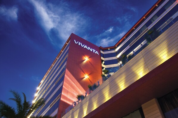 Un hotel moderno con un llamativo letrero de 'VIVANTA', que presenta un diseño arquitectónico único con fachada roja y varios balcones.