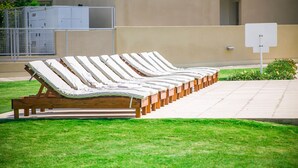 A row of wooden lounge chairs with cushions, arranged outdoors on a grassy area.