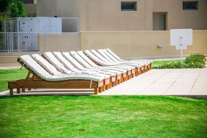 Una hilera de sillones de madera con cojines, ubicados al aire libre sobre un césped.
