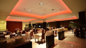 A spacious hotel lobby with multiple dining areas, a reception desk, and a large potted plant.