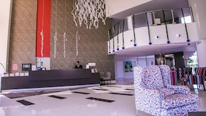 A modern hotel lobby with a reception desk, a patterned armchair, and a decorative ceiling installation.