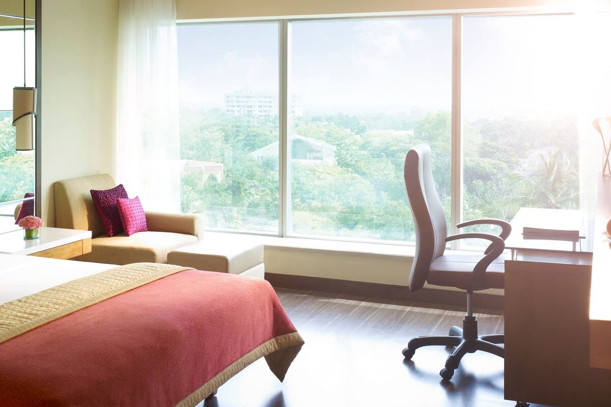 Quarto de hotel com uma janela grande, uma cama, uma mesa e uma cadeira.