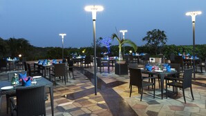An outdoor dining area with tables and chairs, illuminated by tall street lamps. - Vivanta Coimbatore (Coimbatore)