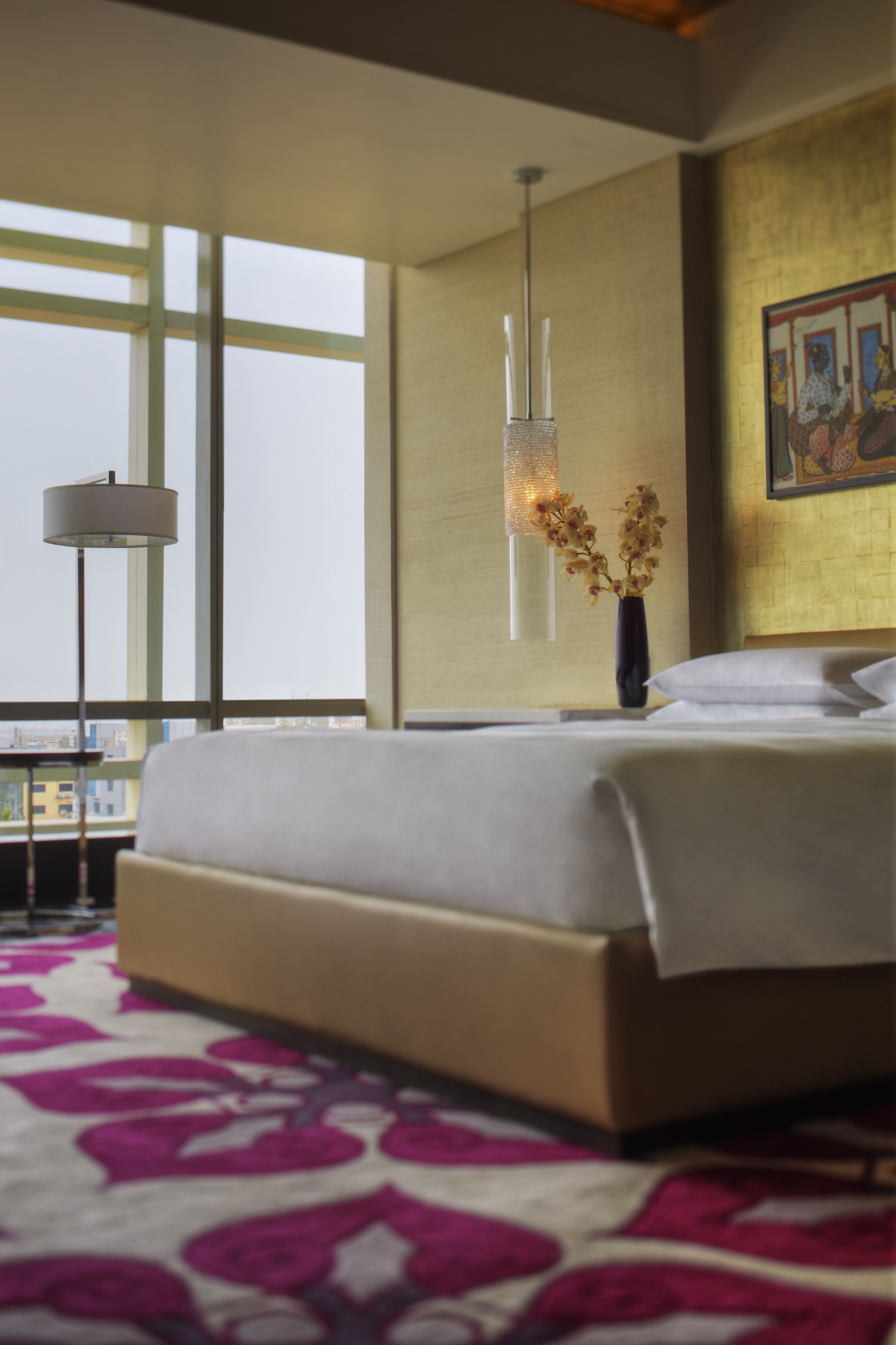 Ein Hotelzimmer mit einem großen Bett, einer Stehlampe, einer Blumenvase und einem Bild an der Wand.