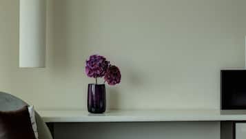 Una sala moderna con un sofá gris, un jarrón con flores moradas, una lámpara colgante blanca y un televisor de pantalla plana sobre una estantería.