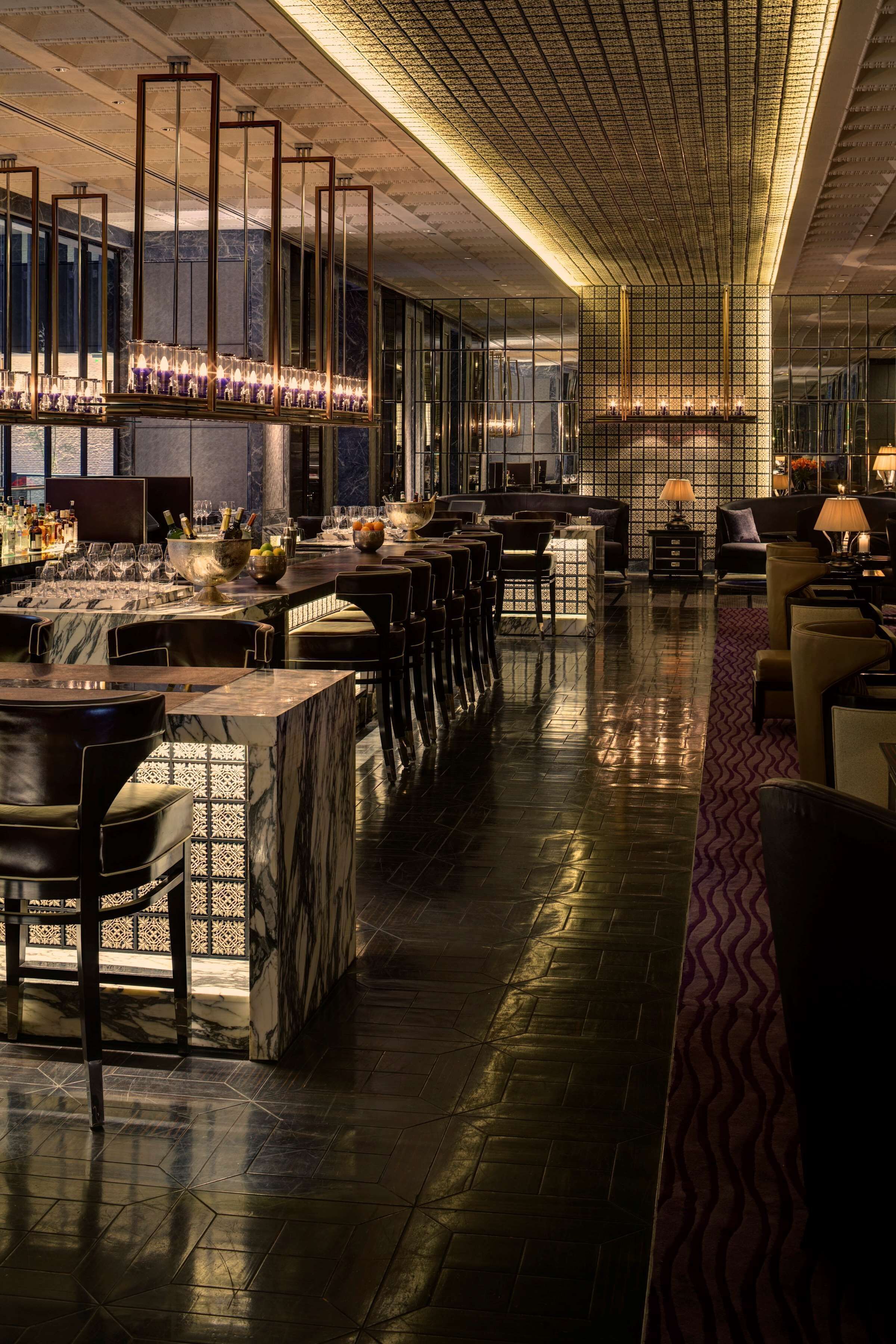 A modern bar area with marble countertops, leather chairs, and a patterned rug.
