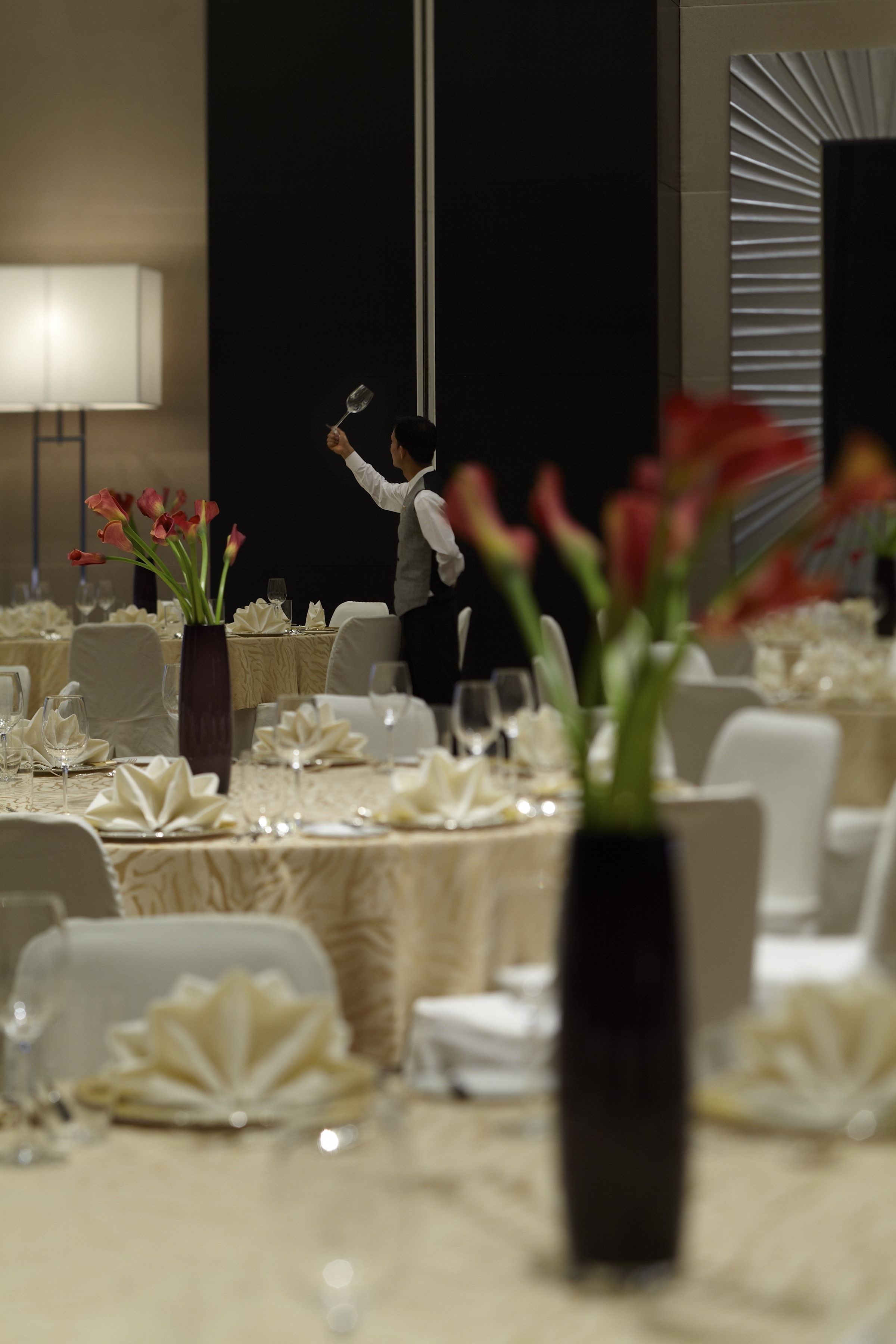 A banquet hall with tables set for a formal event, featuring a central vase with flowers.