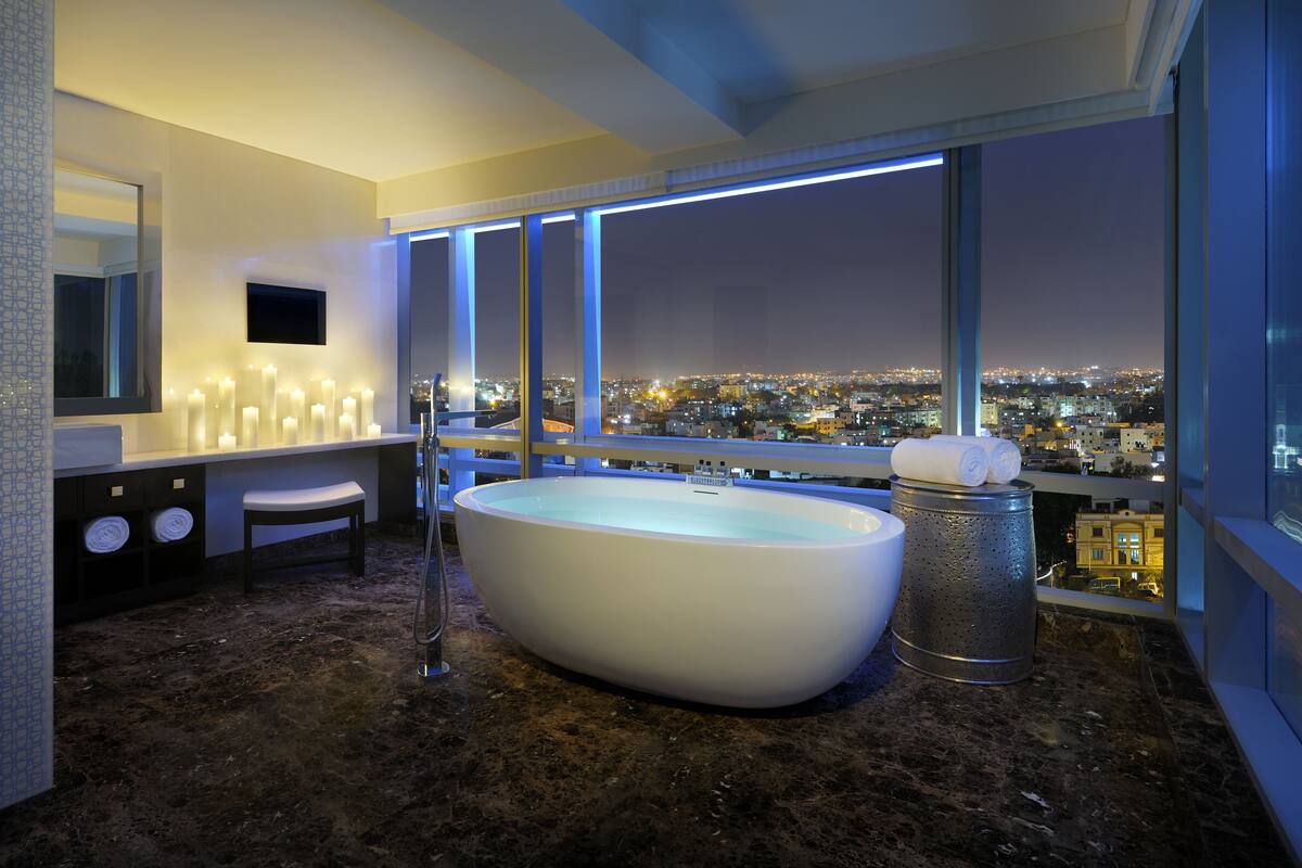 Une salle de bain moderne avec une grande baignoire, un meuble-lavabo avec un miroir et une vue sur le paysage urbain la nuit.