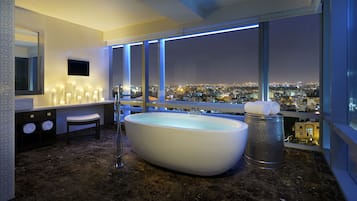 A modern bathroom with a large bathtub, a vanity with a mirror, and a view of a cityscape at night.