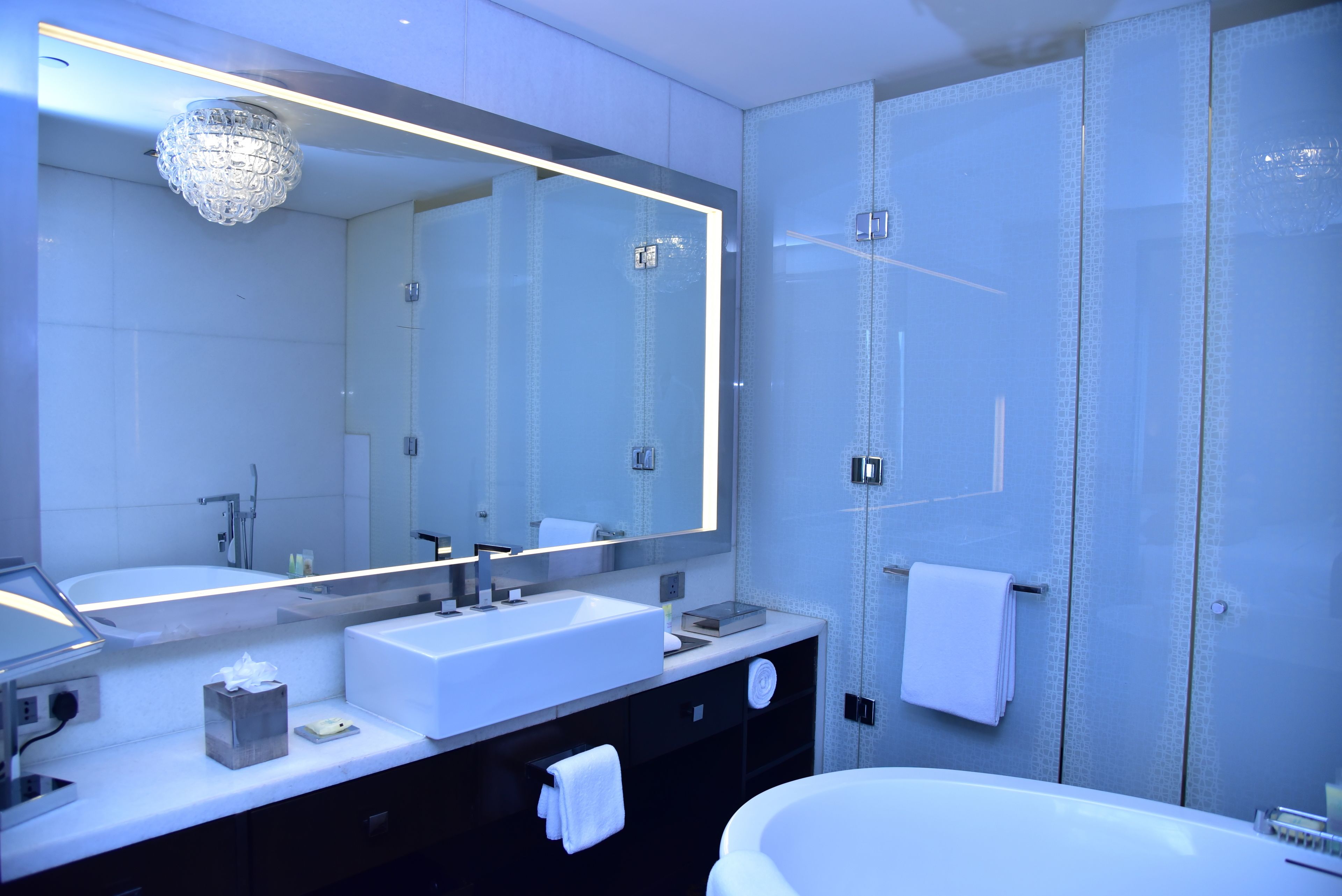 A modern bathroom with a large mirror, two sinks, a bathtub, and a towel rack.