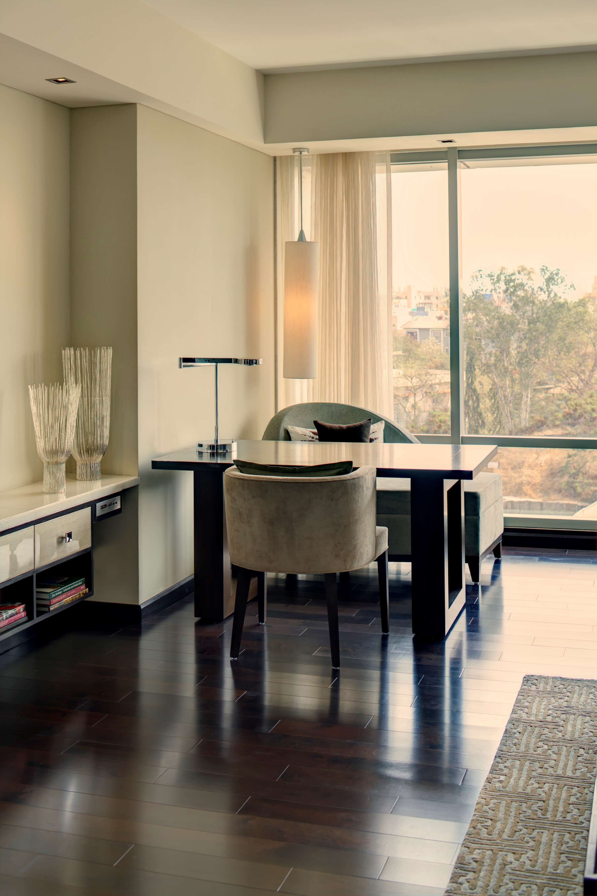 A modern hotel room with a large window, a desk, a chair, and a floor lamp.