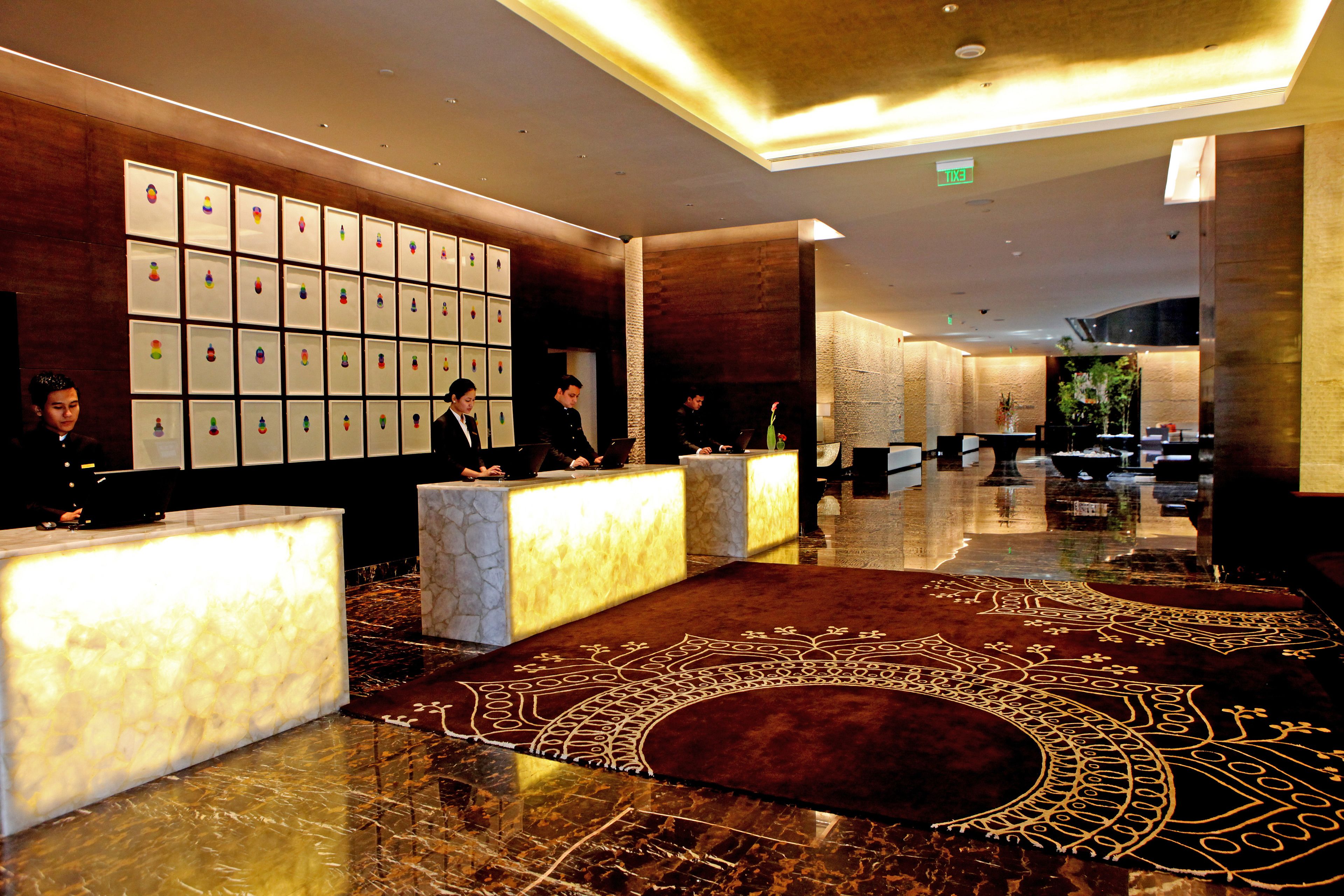 A hotel lobby with marble reception desks, a patterned carpet, and framed artwork on the wall.