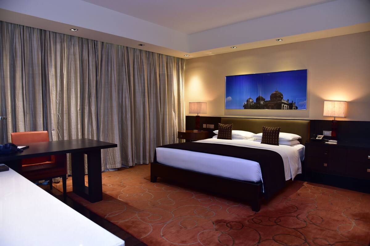 Une chambre d’hôtel avec un lit, un bureau, une chaise, une table de chevet et un tableau au mur.