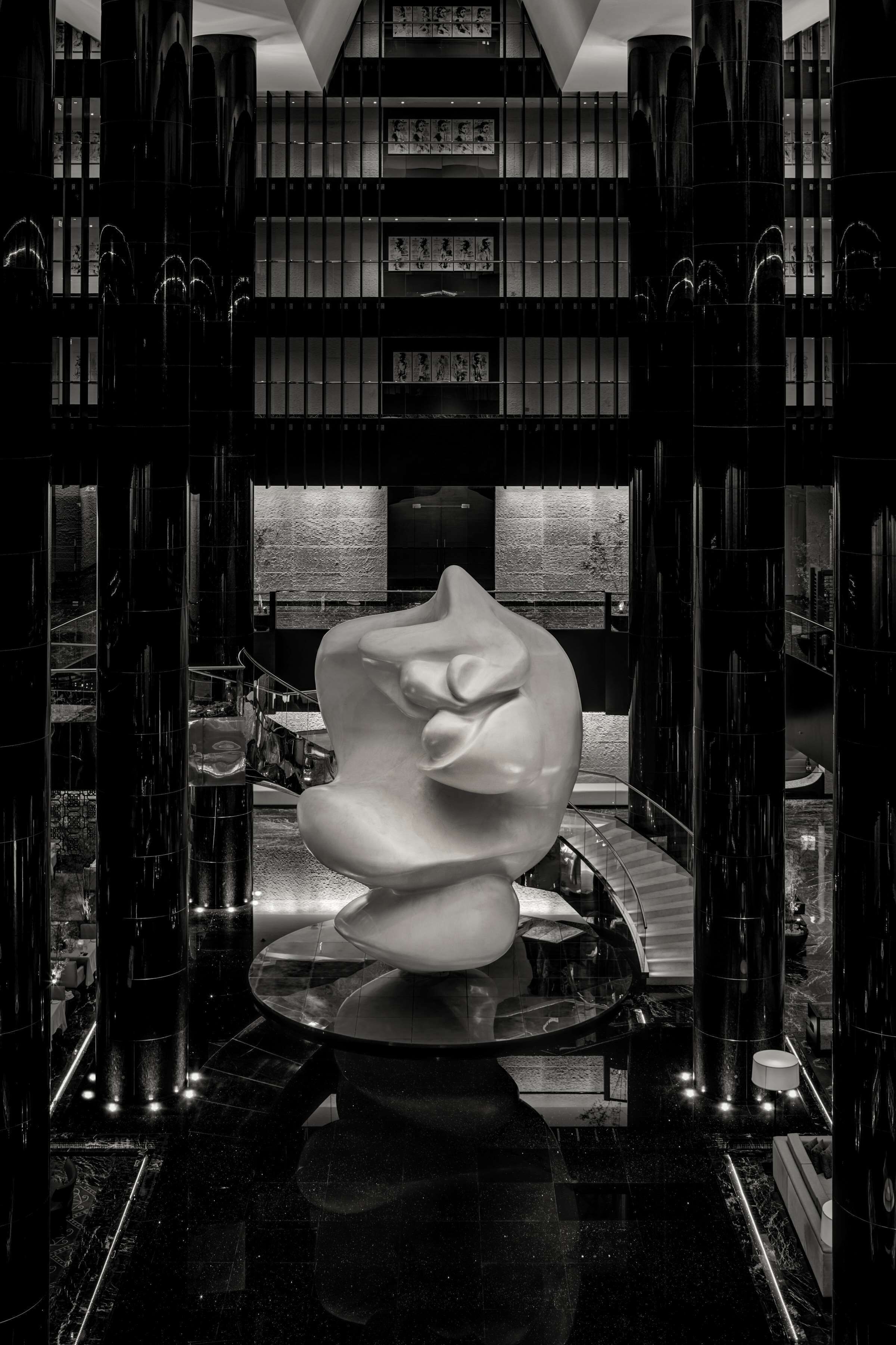 A modern lobby with a central sculpture, high ceilings, and a series of framed artworks on the walls.