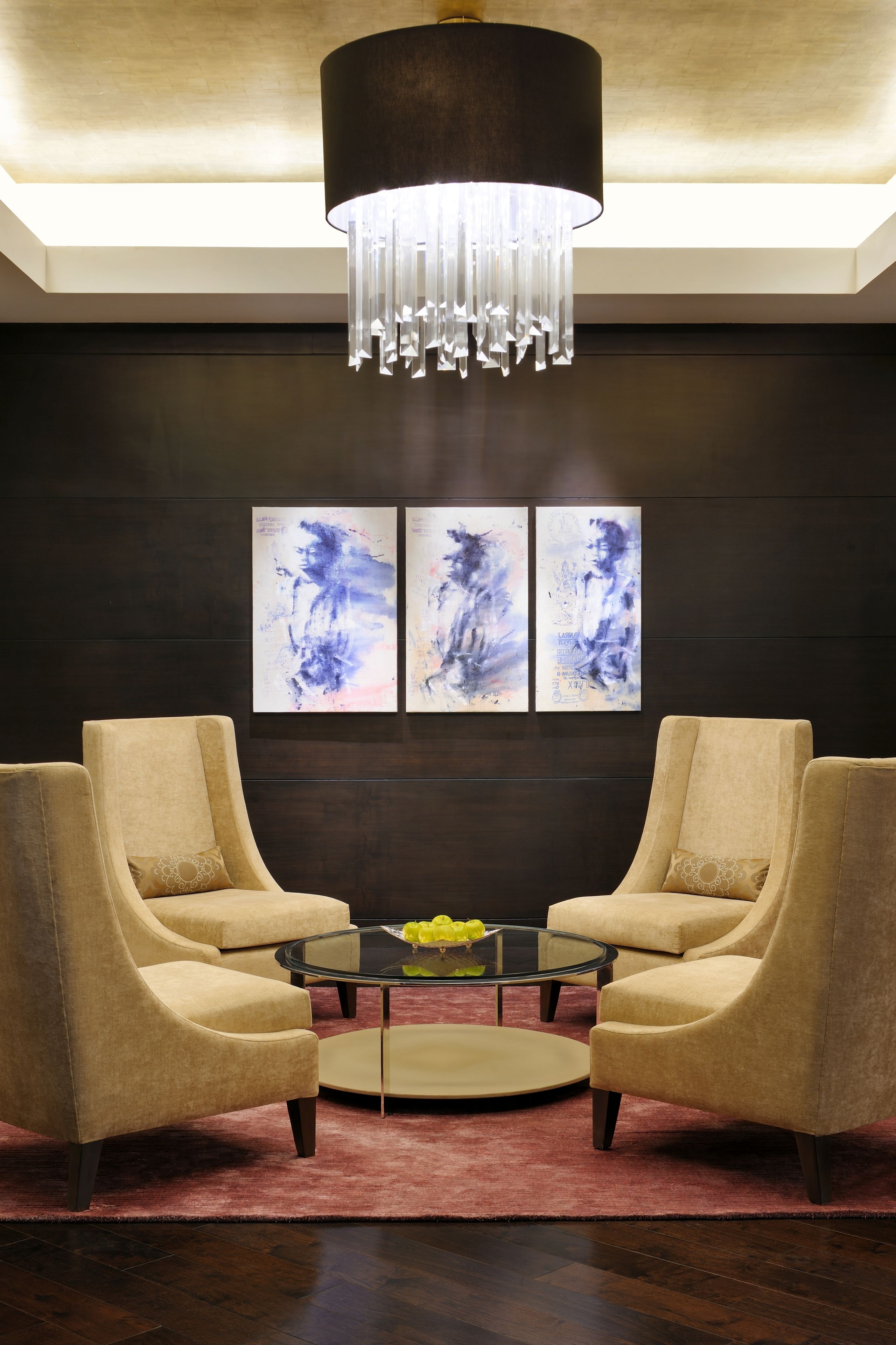 A modern living room with two beige armchairs, a glass coffee table, and a large chandelier.