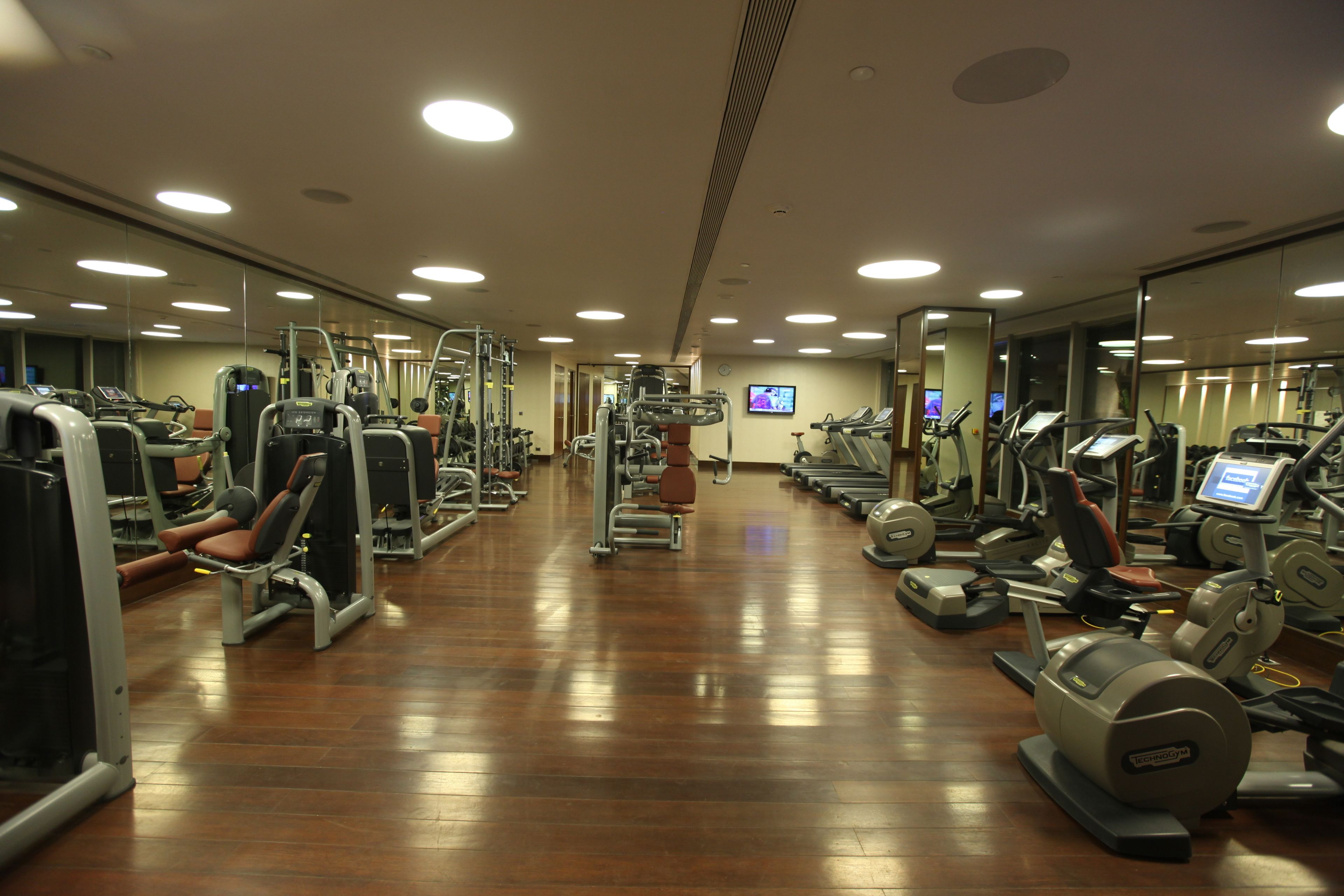 Un gimnasio con diferentes máquinas de ejercicio, espejos y una pantalla de televisión.